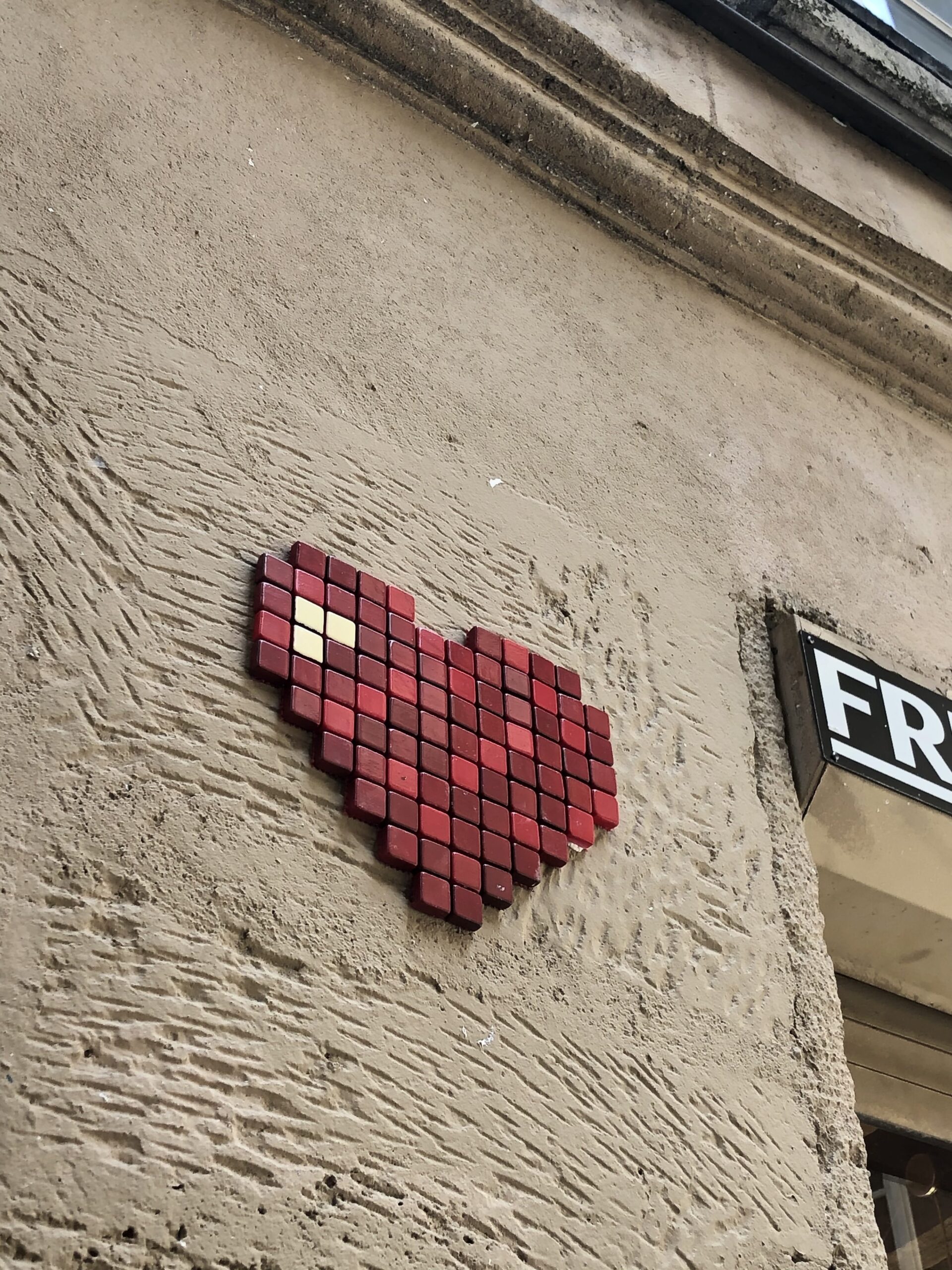 image street art Un coeur rouge en Pixel art sur un mur jaune dans la rue